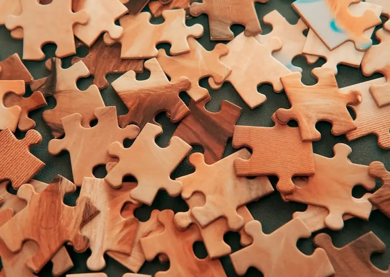 Bringing together the right pieces for an effective CRM strategy. Scattered wooden puzzle pieces representing the complexities of CRM strategy and system integration.