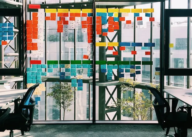 Visualizing project management with structured planning and organization. A glass wall covered in colorful sticky notes, illustrating project planning, task organization, and agile workflows.